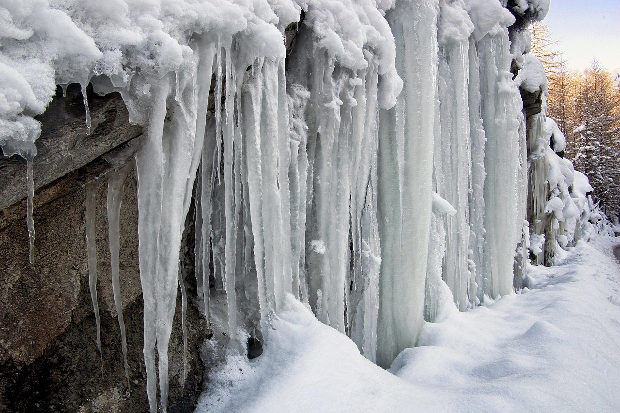 Cascata ghiacciata in inverno, alta e maestosa, circondata da paesaggi innevati.