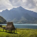 Vista panoramica del lago, circondato da montagne e vegetazione, simile a un fiordo norvegese.