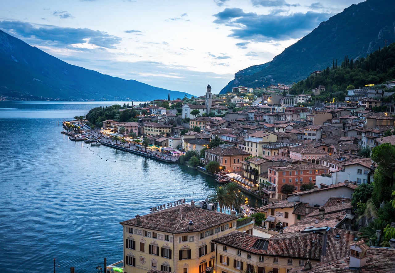Vista panoramica di Riva del Garda con lago, montagne e architettura storica in una giornata estiva soleggiata.