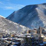 Panorama di un suggestivo borgo di montagna innevato, con case in legno e alberi coperti di neve.